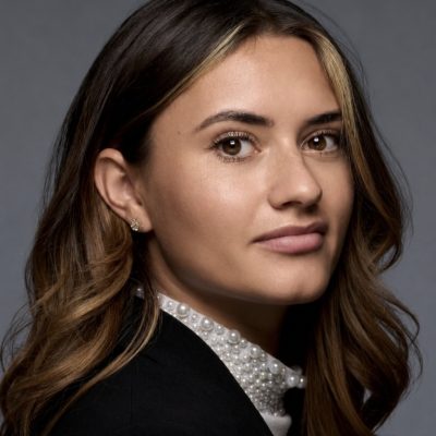 side profile headshot photo of young professional woman with dark hair in a dark jacket with a white shirt collar covered in pearls